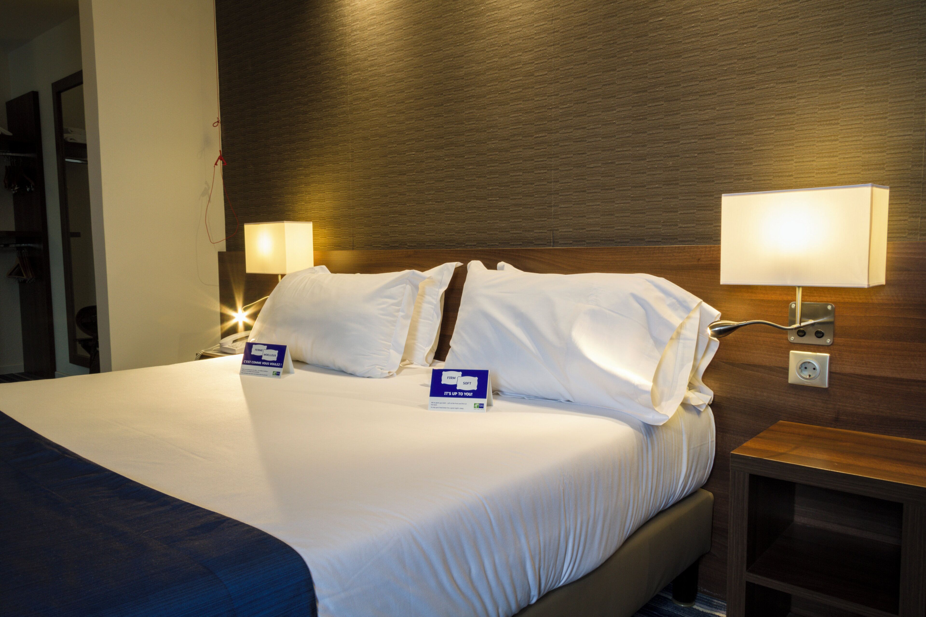 Una camera d'albergo con un letto rifatto, due abat-jour, un comodino e una presa di corrente a muro.
