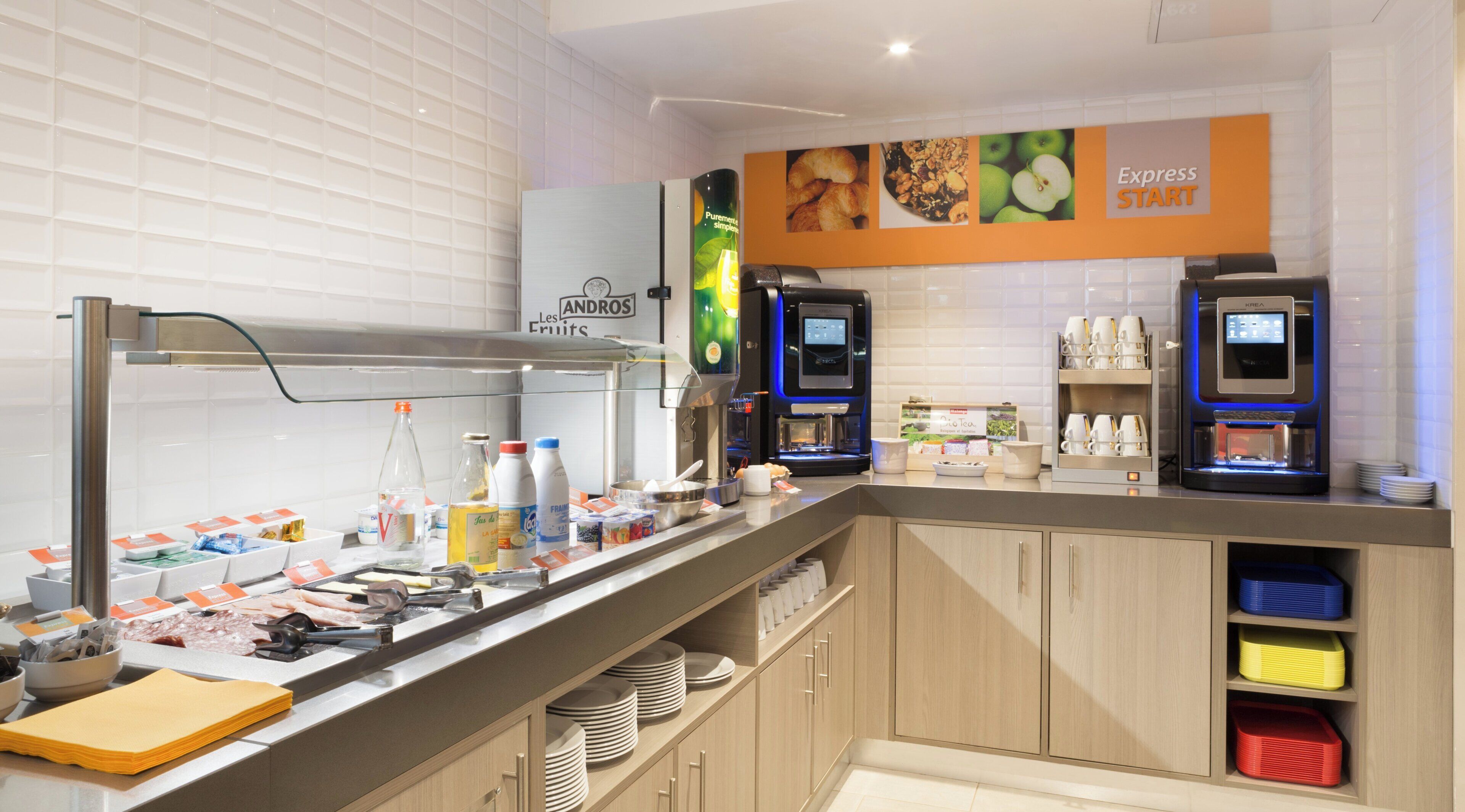 A self-service breakfast area with a coffee machine, milk dispensers, and a variety of food items.
