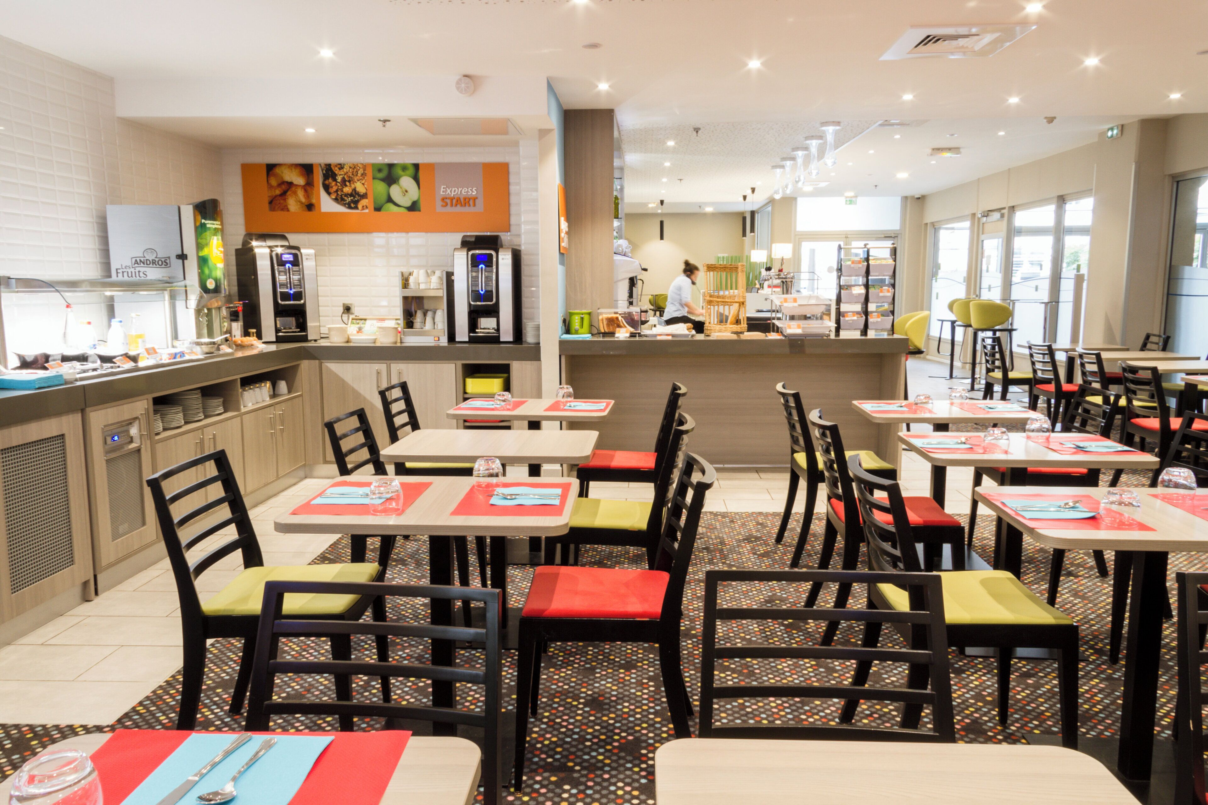Un restaurante con varias mesas y sillas, una barra con dispensador de bebidas y un tablero de menú.