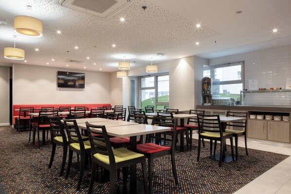 A modern dining area with multiple tables and chairs, a kitchen area, and a view of the outside. - Holiday Inn Express Amiens by IHG (Amiens)