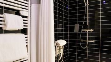 Ein modernes Badezimmer mit schwarzem Fliesenbelag, einem weißen Handtuchhalter, einer Dusche mit Duschbrause und einem WC mit Papierhandtuchhalter.