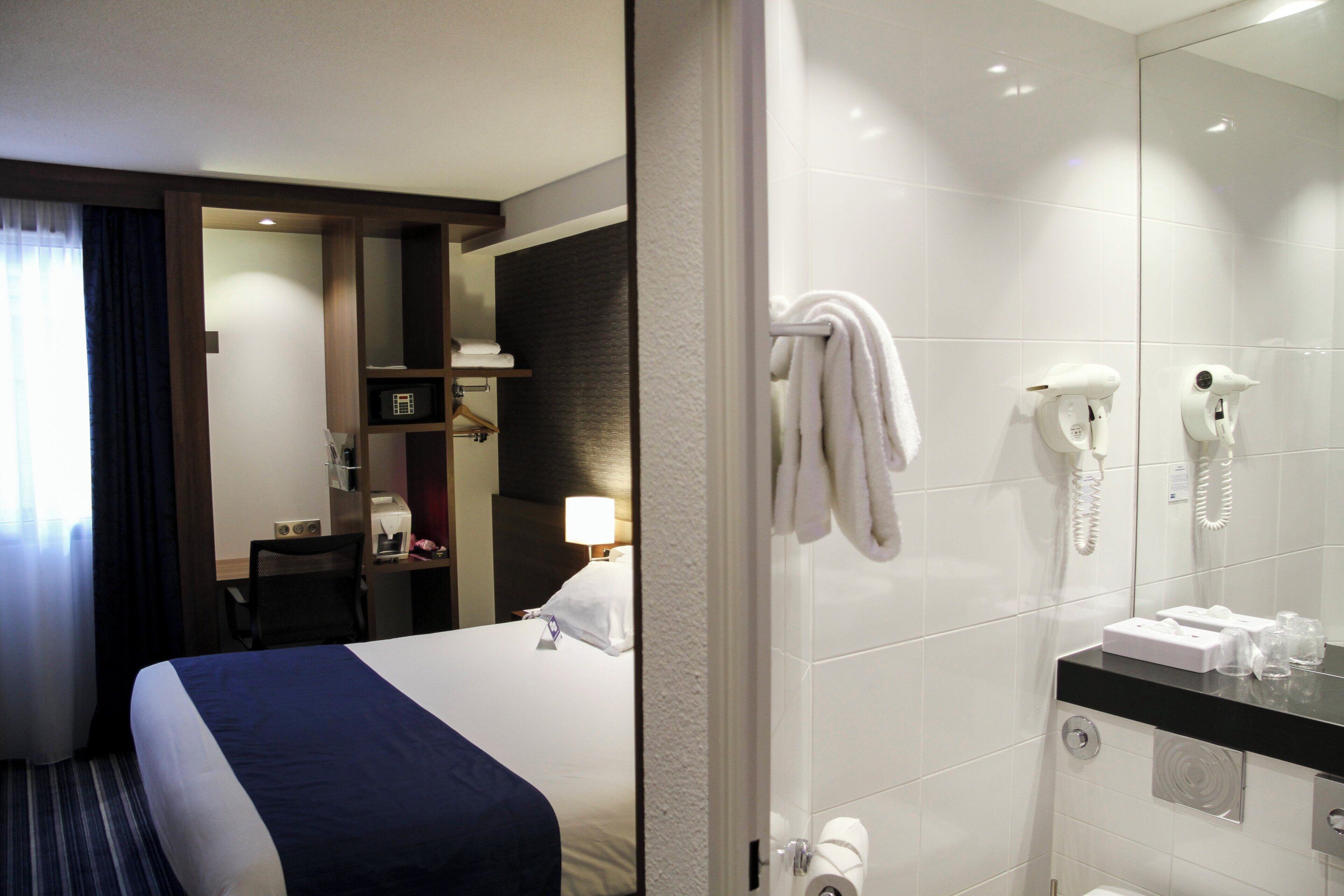 Ein Hotelzimmer mit Bett, Schreibtisch, Stuhl, Badezimmer mit Dusche, Handtuchhalter und Telefon.