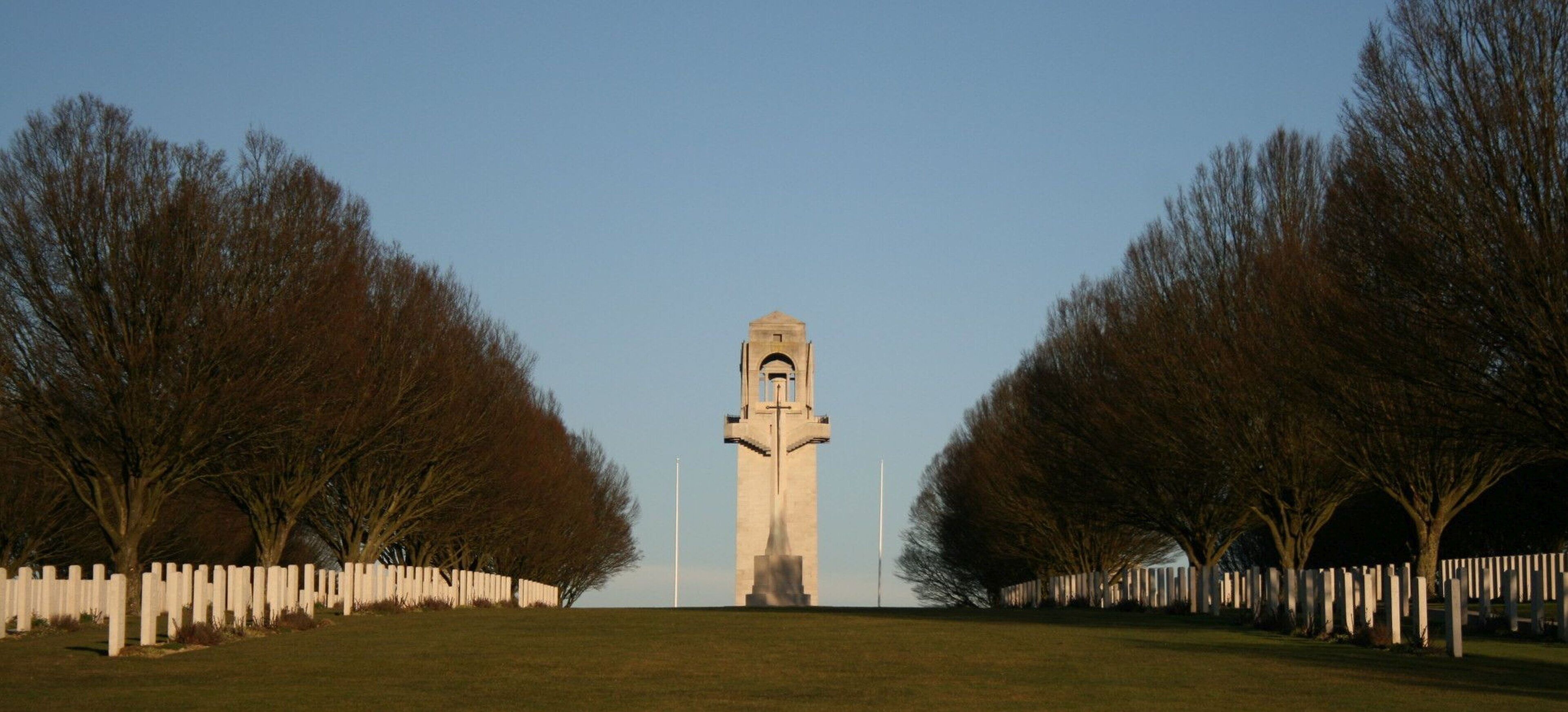 A tall monument with a clock tower, surrounded by a white fence and trees.