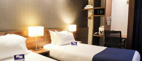 Une chambre d’hôtel avec deux lits, chacun étant équipé d’un oreiller et d’une table de chevet avec une lampe. On y trouve également un bureau avec une chaise et un four à micro-ondes.