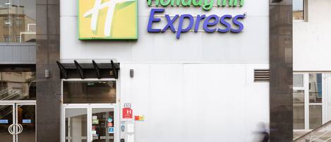 A Holiday Inn Express sign with a green and yellow logo, a glass entrance, and a bicycle parked outside.