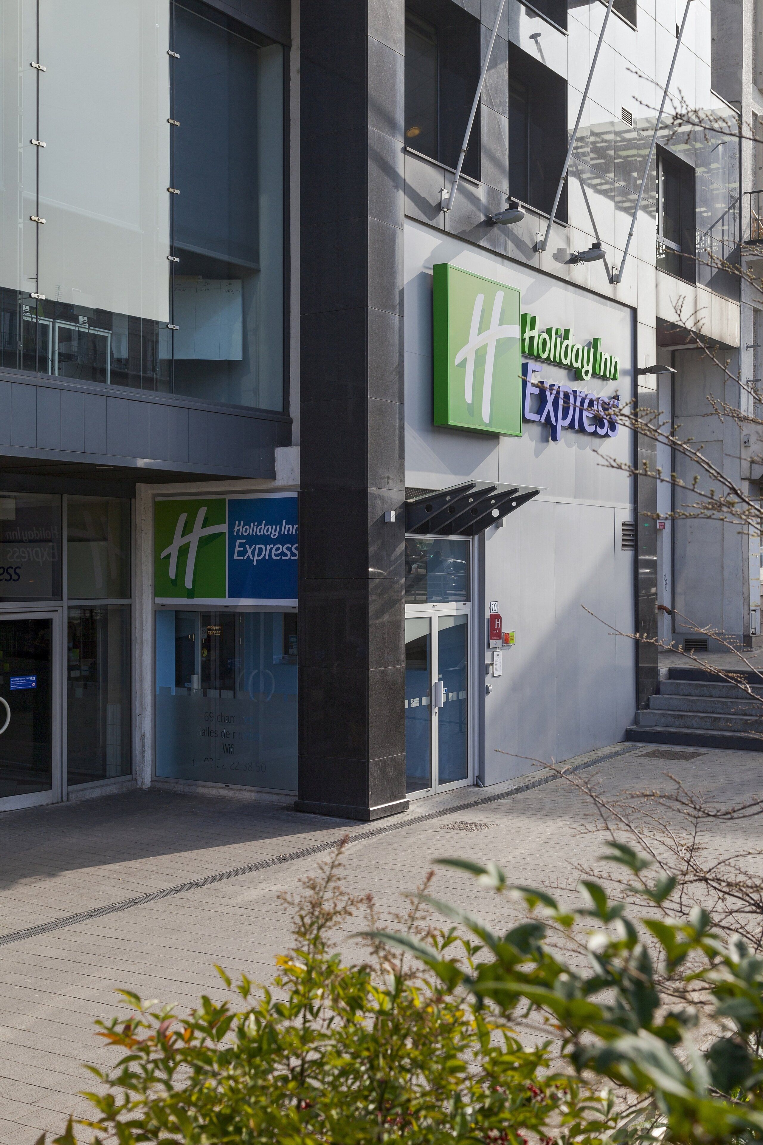 A Holiday Inn Express building with a glass facade, a visible entrance, and a fire alarm box.