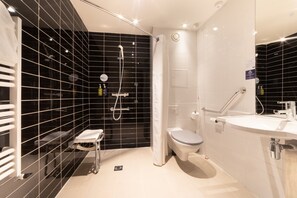 A modern bathroom with a black-tiled shower area, a white toilet, and a sink with a mirror.