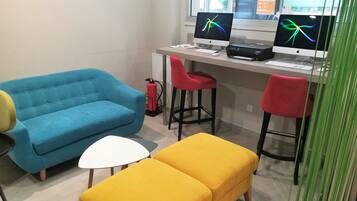 A workspace with a desk, two monitors, a blue sofa, a yellow ottoman, and red chairs.