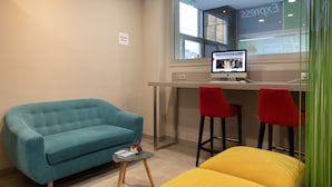 A modern office space with a teal sofa, a yellow ottoman, and red bar stools.