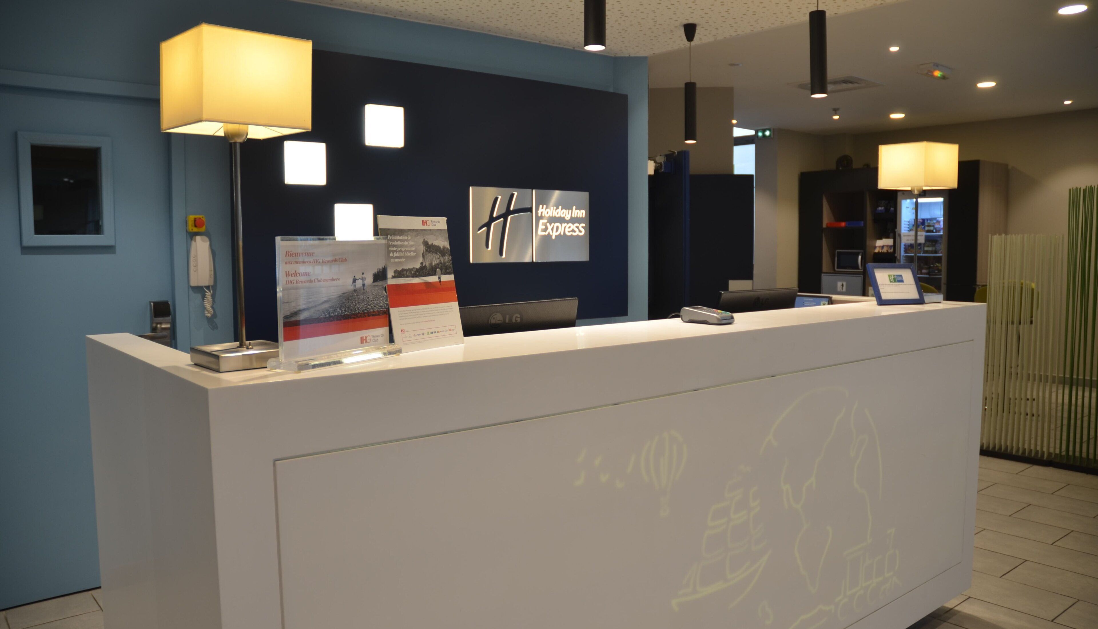 Ein Empfangsschalter mit blauer Wand, einem Telefon, einem digitalen Display und einem Schild für Holiday Inn Express.