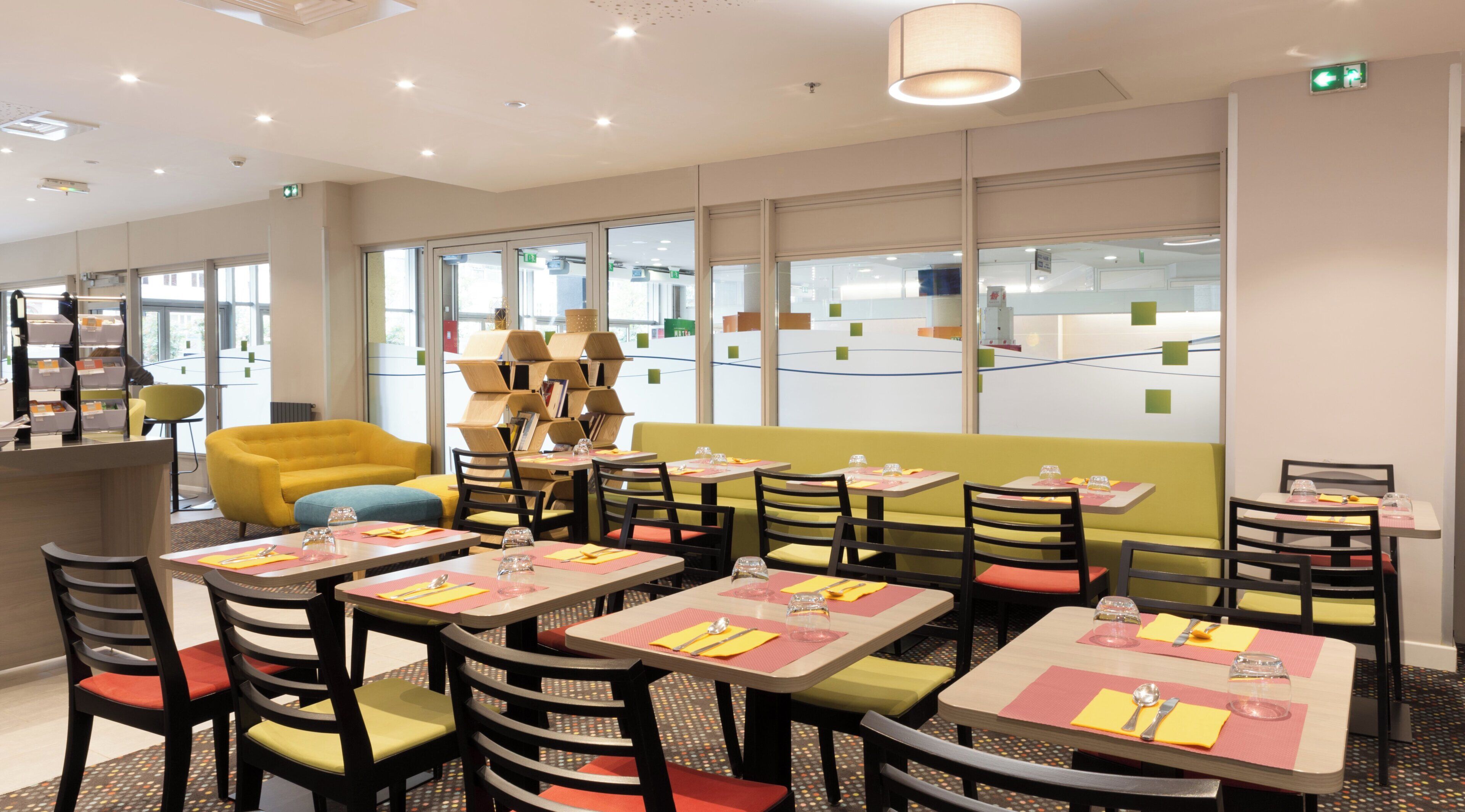 Un restaurant avec plusieurs tables et chaises, un canapé jaune et une grande fenêtre donnant sur un beau paysage.