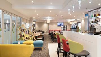 A hotel dining area with multiple tables and chairs, a bar, and a television screen.