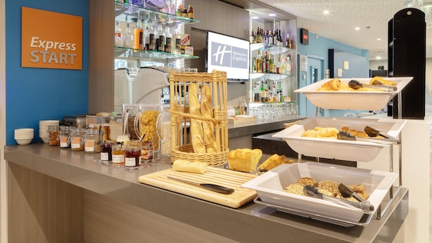 A hotel breakfast buffet with various food items, a wicker basket with baguettes, and a sign that reads "Express START".