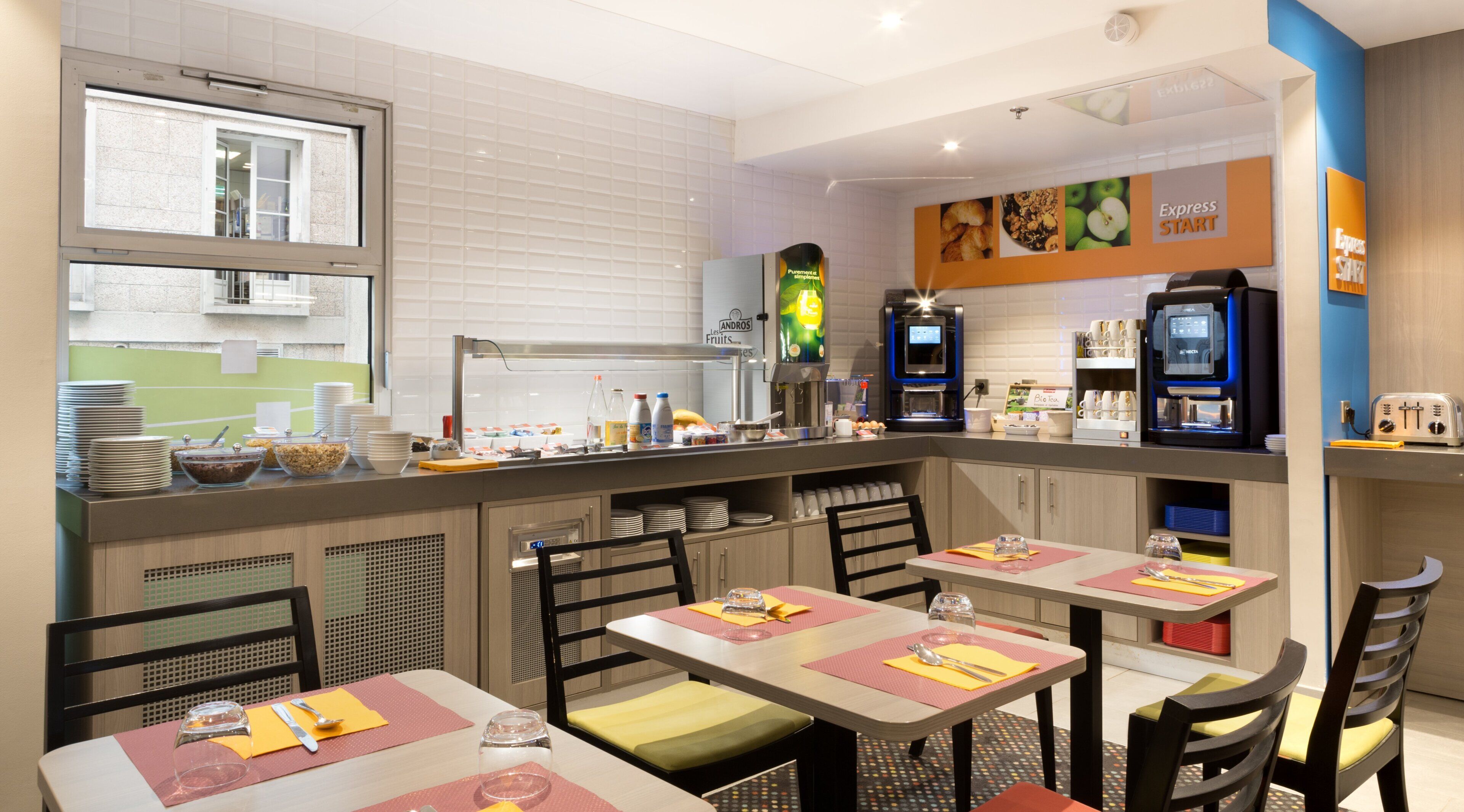 Zona de desayuno con servicio de buffet, mesas y máquinas de café.