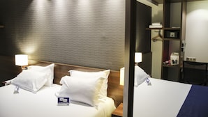 A hotel room with a large bed, two bedside lamps, a wooden headboard, a mirror, a desk with a chair, and a microwave.