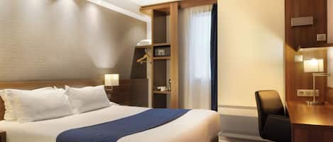 A hotel room with a large bed, bedside tables, a desk with a chair, a wardrobe, and a window with curtains.