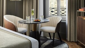 Una habitación moderna con una mesa redonda, dos sillas, una lámpara de pie y vistas a edificios a través de un balcón con ventanal.