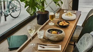 Una mesa de comedor con una bandeja que contiene una copa de vino blanco, un plato de comida y un recipiente pequeño de pasta.