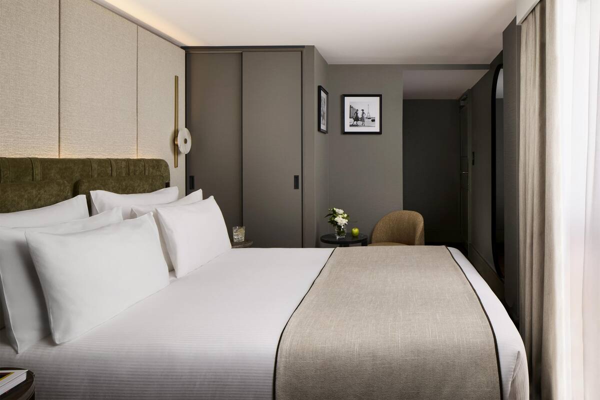 A hotel room with a large bed, a headboard, a bedside table with a vase of flowers, and a framed picture on the wall.