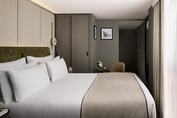 A hotel room with a large bed, a headboard, a bedside table with a vase of flowers, and a framed picture on the wall.