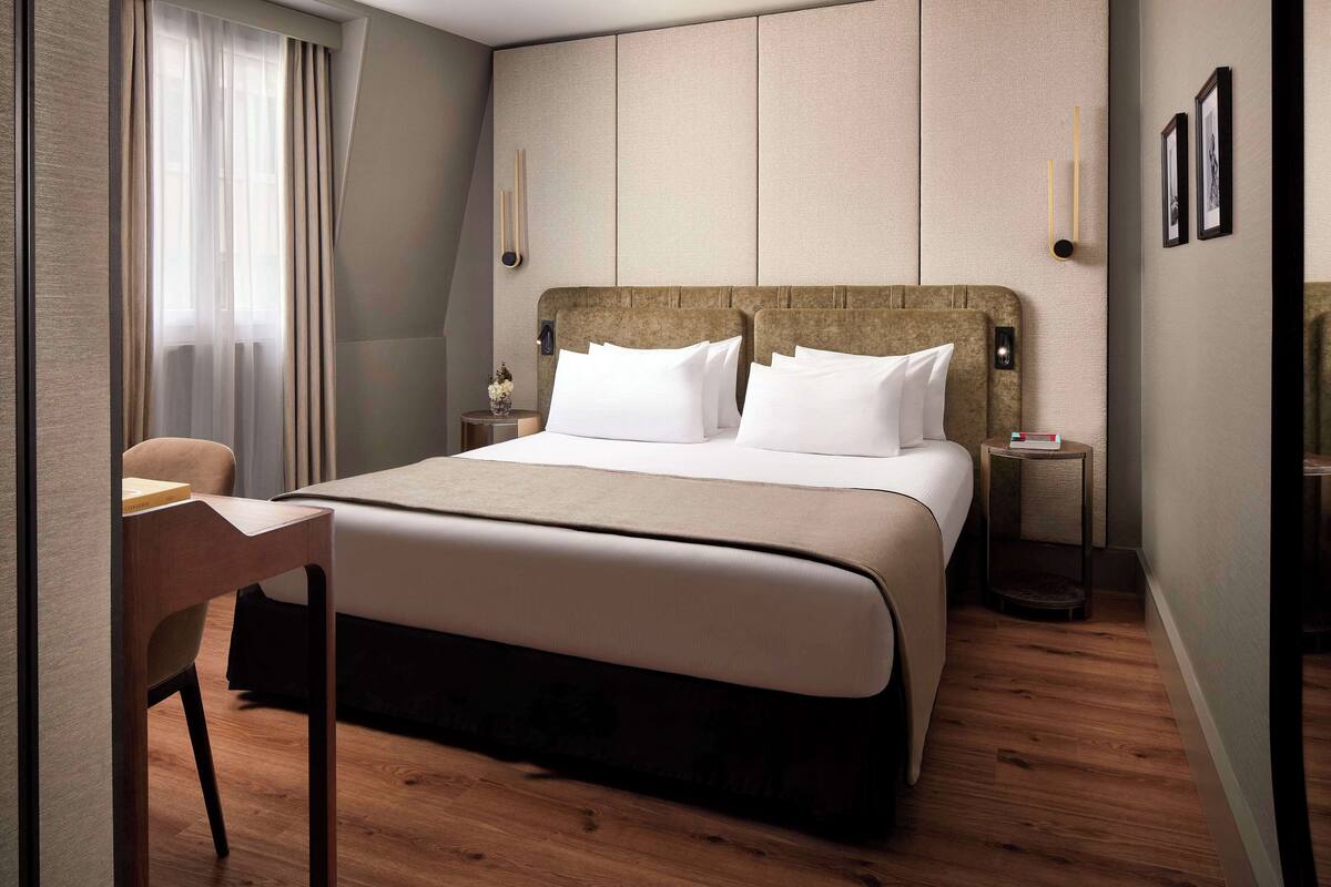A modern hotel room with a large bed, a desk, and a chair.