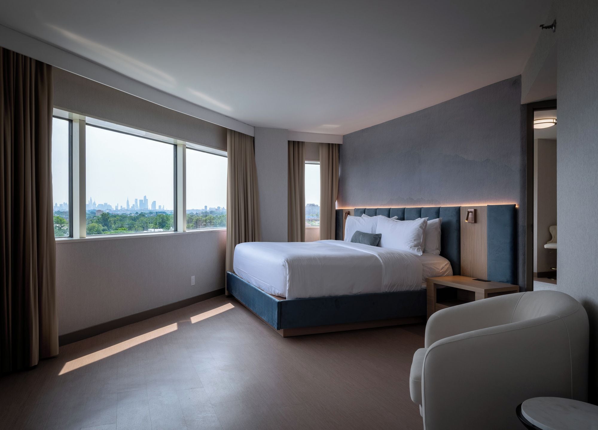 A hotel room with a large bed, a seating area, and a view of a city skyline.