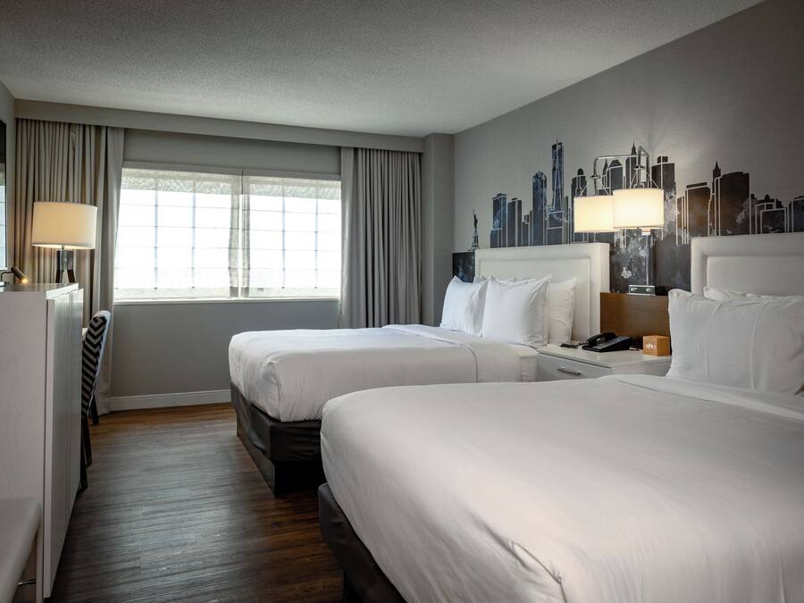 Ein Hotelzimmer mit zwei Betten, einem Schreibtisch, einem Sessel und einer Wandmalerei mit Stadtansicht.