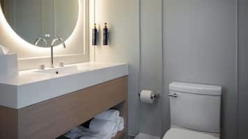 A modern bathroom with a round mirror, a white sink, a toilet, and a shelf with towels.