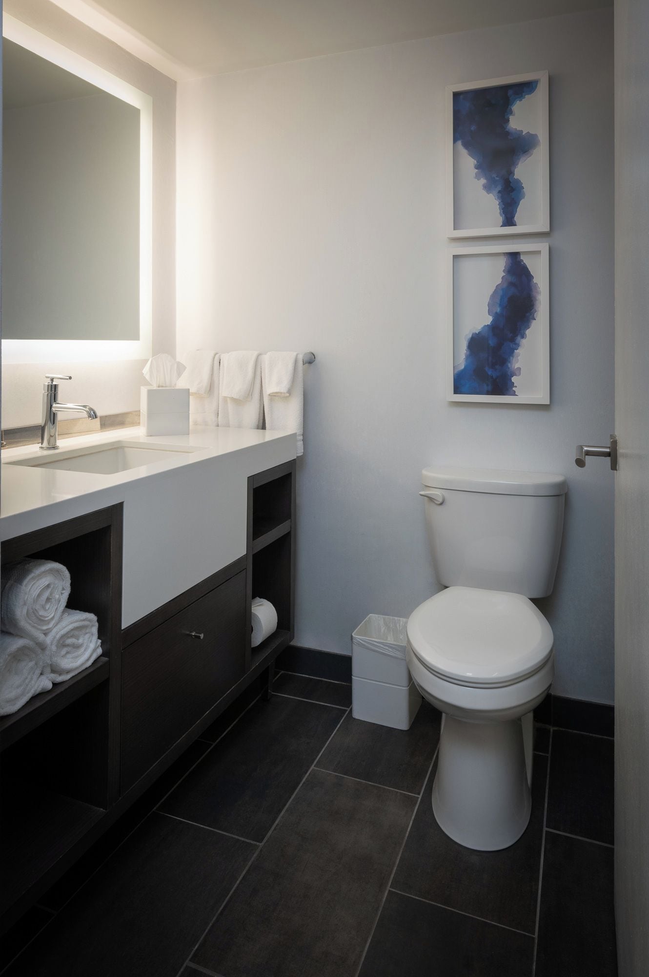 A modern bathroom with a white sink, dark cabinetry, a toilet, and abstract art on the wall.