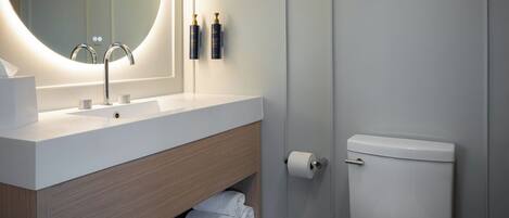 Un baño moderno con un espejo redondo, un lavabo blanco, un inodoro y un estante con toallas.