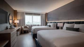 A hotel room with two beds, a desk, a chair, and a large window with curtains.
