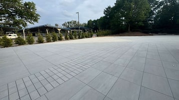 A spacious outdoor area with a tiled floor, covered seating, and trees in the background.