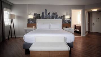 A hotel room with a large bed, bedside tables, a cityscape mural, a floor lamp, and a bedside phone.
