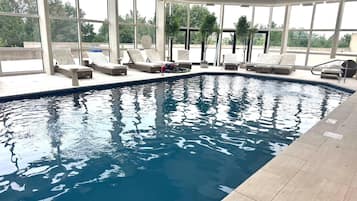 Une piscine intérieure à l’eau d’un bleu cristallin, entourée de chaises longues et d’un espace salon abrité.