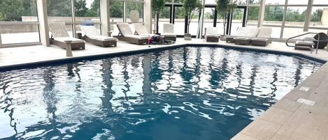 An indoor swimming pool with clear blue water, surrounded by lounge chairs and a covered seating area.
