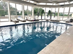 An indoor swimming pool with clear blue water, surrounded by lounge chairs and a covered seating area. - World of Blue (East Rutherford)