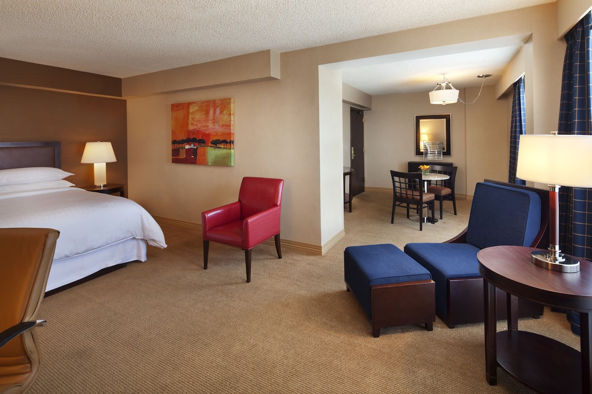 Habitación de hotel con una cama, una silla roja, un sofá azul, una mesita y un escritorio con una silla.