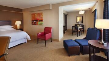 A hotel room with a bed, a red chair, a blue sofa, a small table, and a desk with a chair.