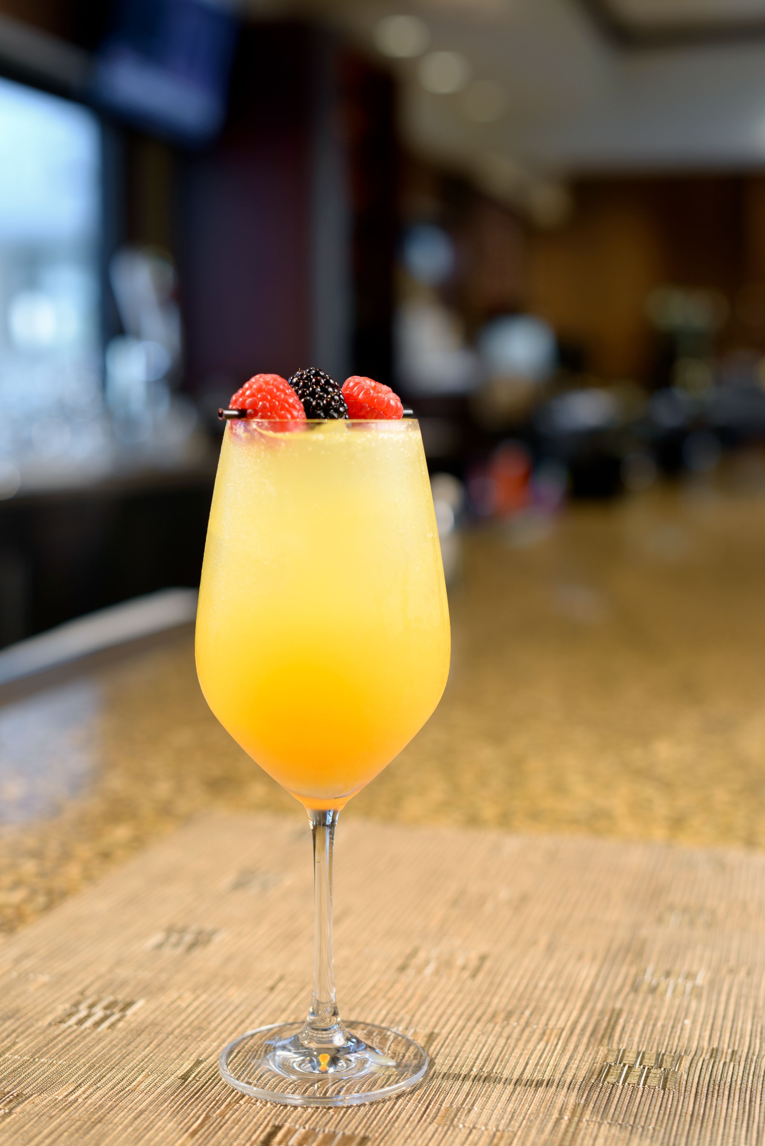 A cocktail glass with a fruit garnish on a wooden bar counter.