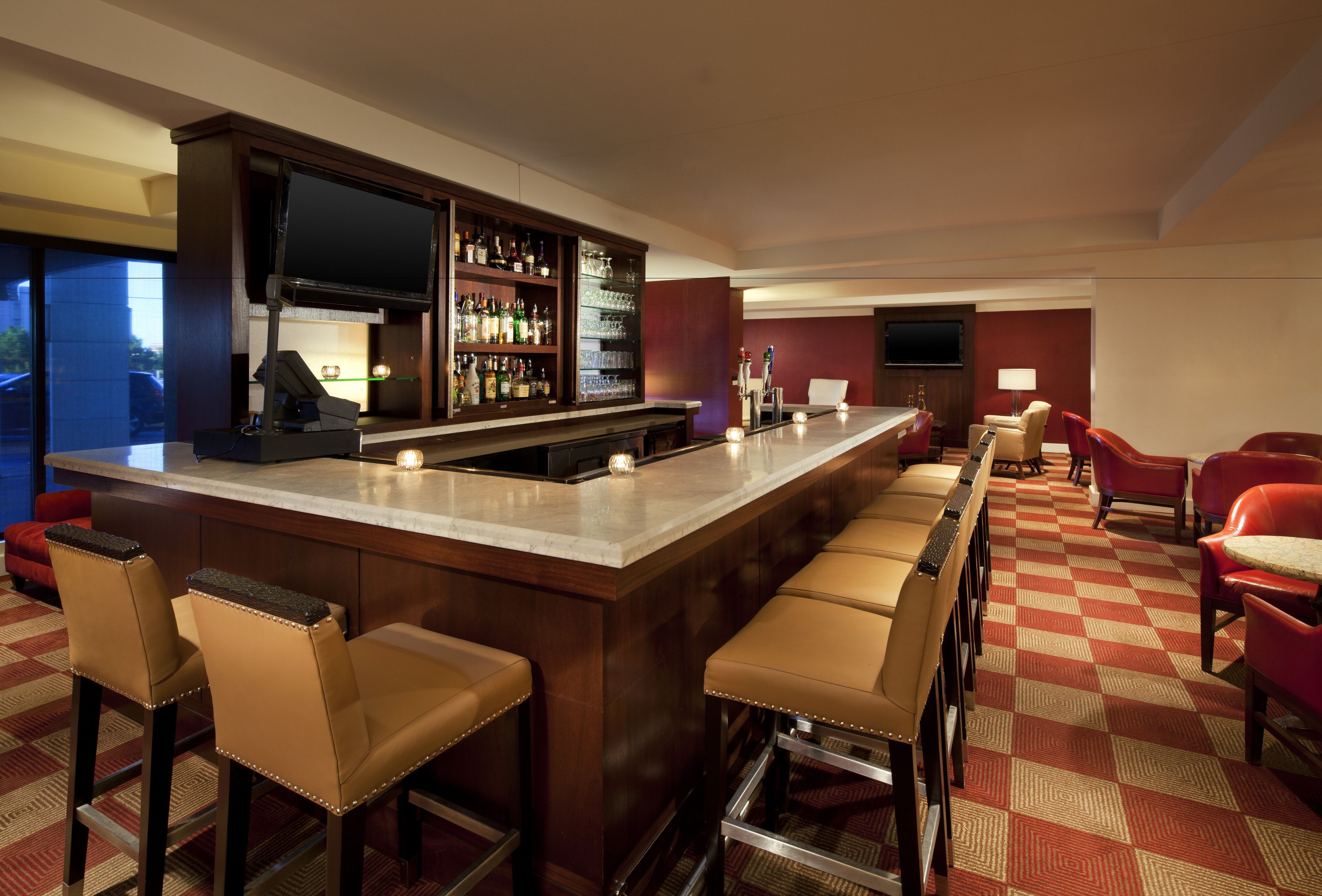 A bar area with a long counter, multiple stools, and a television screen.