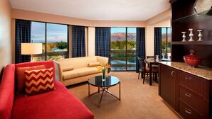 Ein Hotelzimmer mit rotem Sofa, beigem Sofa, einem Essbereich und Bergblick durch große Fenster.