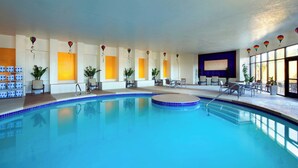 Ein Hallenbad mit klarem, blauen Wasser, umgeben von Liegestühlen und Topfpflanzen.