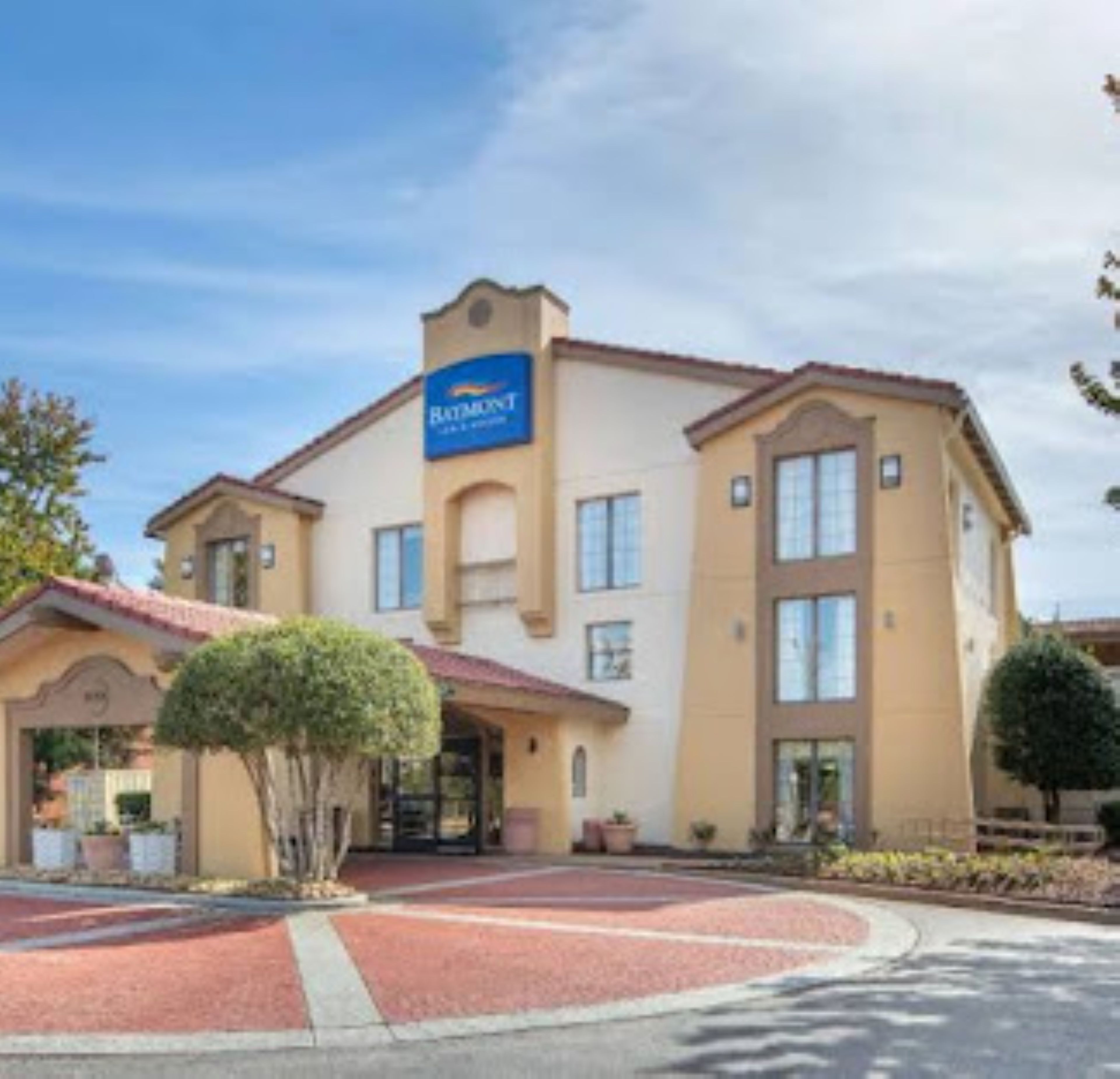 A hotel with a prominent sign, a covered entrance, and a landscaped area with trees.