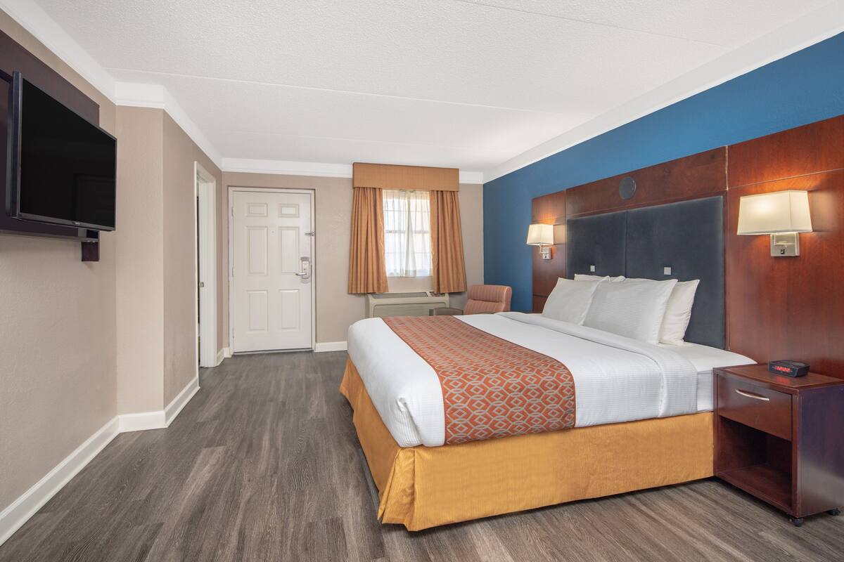 Una habitación de hotel con cama, mesita de noche, lámpara y televisión en la pared.