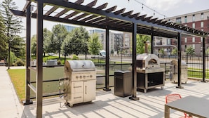 Un patio exterior con una pérgola, dos parrillas y una zona de estar.