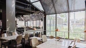 Un restaurante moderno con techos altos, ventanas amplias y vistas a la ciudad. Mesas y sillas dispuestas para comer.