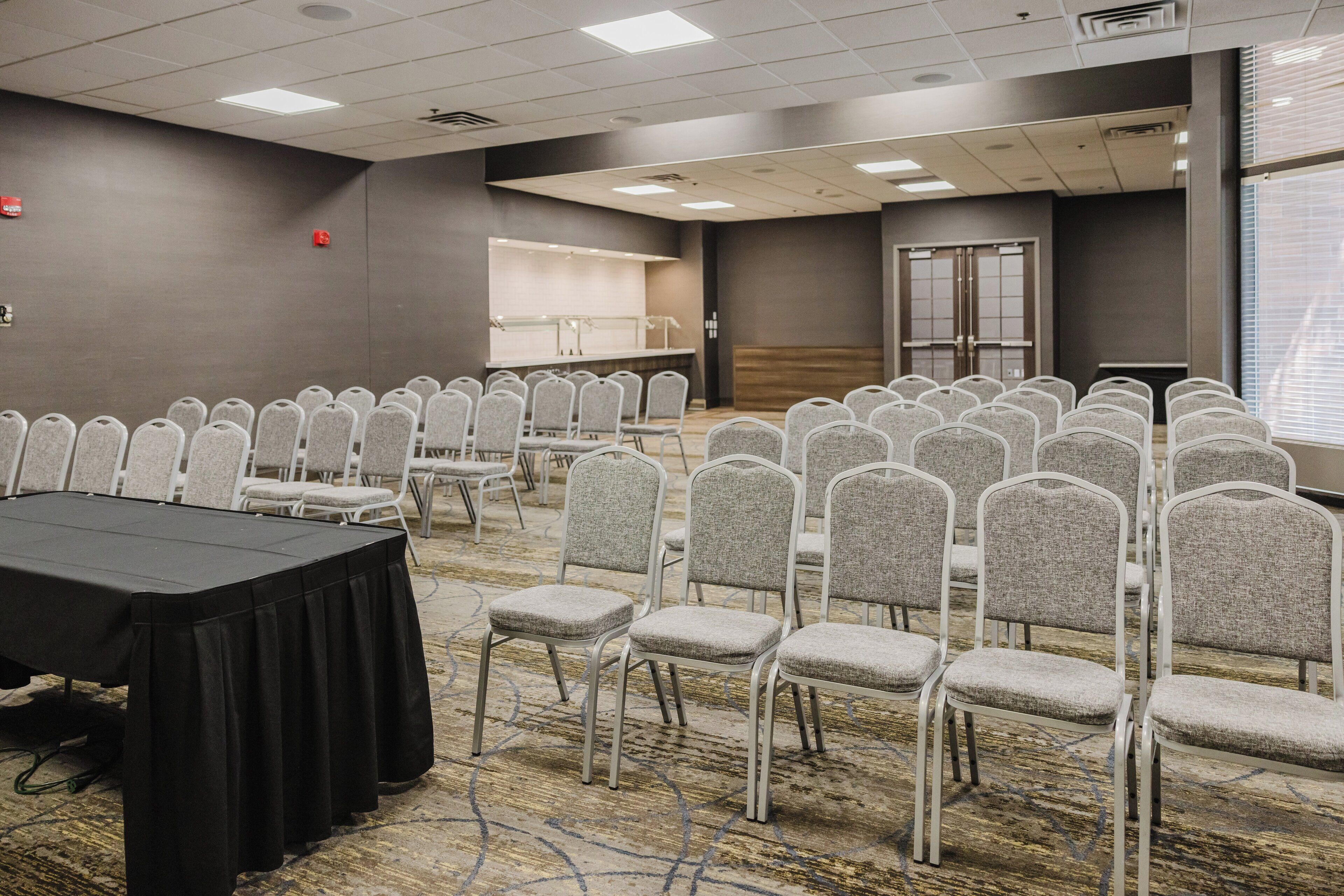 Un salón de conferencias con filas de sillas, una mesa y un ventanal grande.