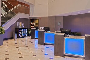 Un hall de hotel con una recepción, una escalera y una máquina expendedora.