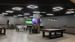 Una sala de billar con mesa de pool, mesa de fútbol de mesa y un televisor mostrando un partido de golf.