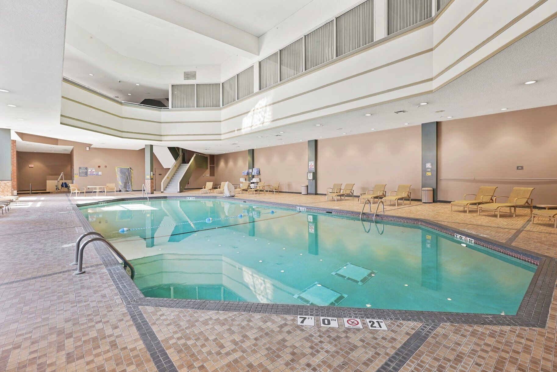 Una amplia piscina interior con una profundidad de 2,13 metros, rodeada de sillas de descanso y una escalera que lleva a un nivel superior.
